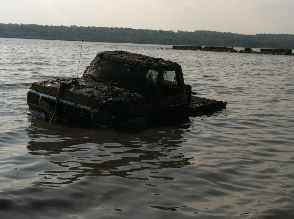 Mud-covered truck partially submerged in water, likely from the 1970s