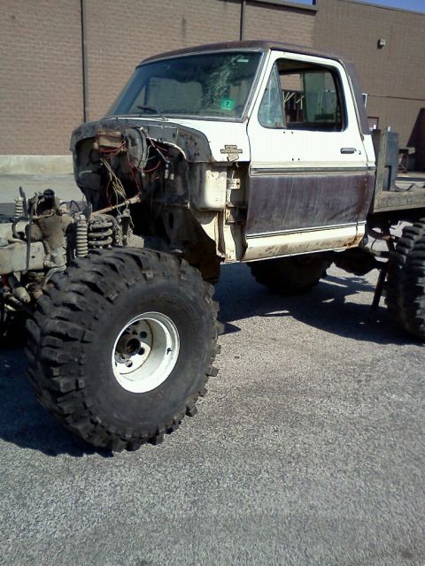 1990 Ford Bronco - This heavily modified pickup truck features oversized tires and a custom flatbed, with its front end partially disassembled.