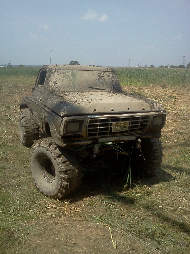 Mud-covered 1979 Ford F-Series truck with large off-road tires parked in a grassy field