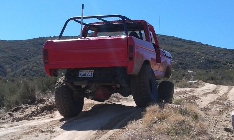 1978 Ford Bronco - Rear view of a red 1978 Ford Bronco modified for off-road use, driving on a dusty trail.