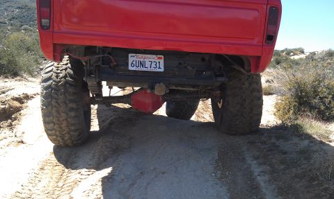 1978 Ford Bronco - Rear view of a red 1978 Ford Bronco on a dirt trail, equipped with off-road tires.