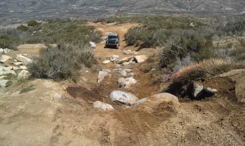 1978 Ford Bronco - A black SUV descends a challenging, rocky off-road path in a dry, mountainous landscape.