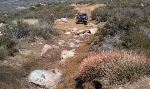 1978 Ford Bronco - A black off-road SUV tackles a challenging, rocky trail in a dry, hilly landscape.