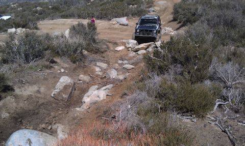 1978 Ford Bronco - SUV with front end damage navigates a challenging rocky trail in a dry, brushy landscape.