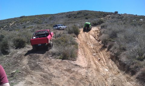 1978 Ford Bronco - Multiple off-road vehicles navigate a challenging dirt path on a sunny day.