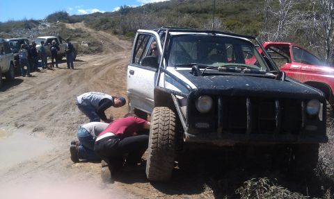 1978 Ford Bronco - Several people attend to a modified off-road vehicle on a dirt track, with other vehicles nearby.