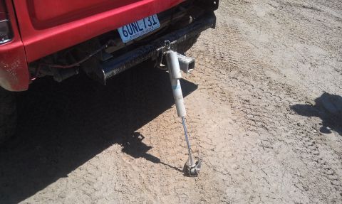 1978 Ford Bronco - A red vehicle's rear bumper and license plate are visible, with a detached shock absorber lying on the ground.