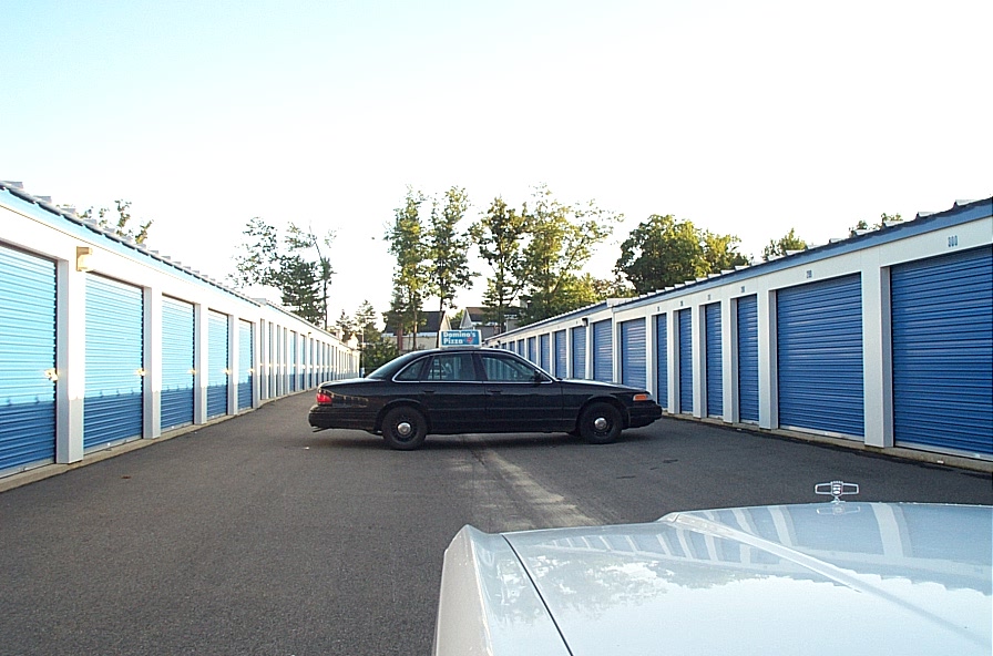 2001 Ford Crown Victoria parked in aisle of storage units, another car's hood in foreground