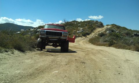 1978 Ford Bronco - A red 1979 Ford F-Series truck navigates a dusty, off-road trail under a bright blue sky.