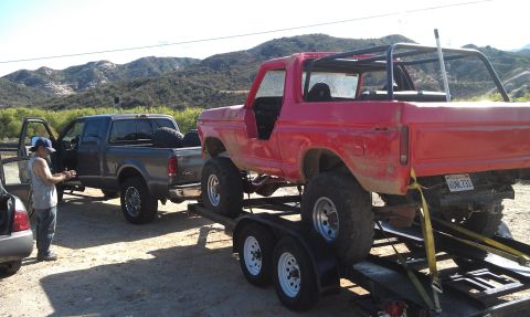 1978 Ford Bronco - A red 1978 Ford Bronco, modified for off-roading with a roll cage, is loaded onto a trailer behind a pickup truck.