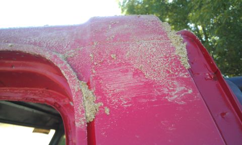 1978 Ford Bronco - Sand covers the exterior of a red vehicle, obscuring details of its body.