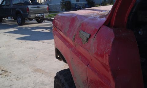 1978 Ford Bronco - Close-up of a red 1978 Ford Bronco fender, showing a dent and the vehicle's badge, with other trucks in the background.