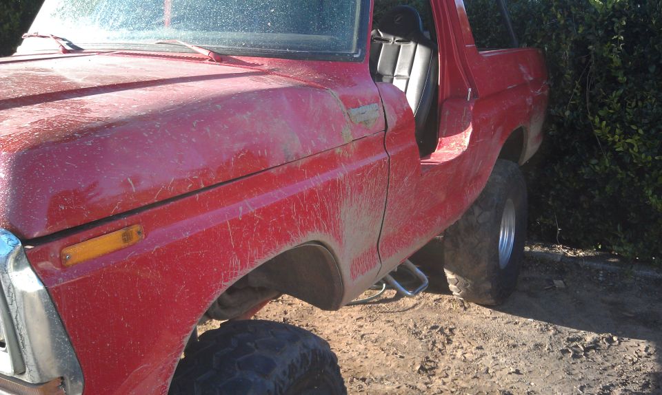 Red 1978 Ford Bronco with door open, parked on dirt