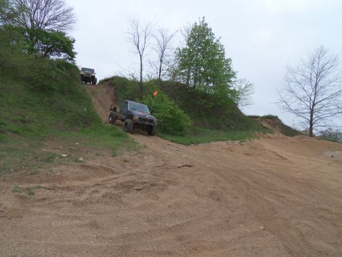 1989 Ford Bronco - Off-road trucks navigate a challenging dirt incline under a cloudy sky.