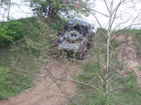 1989 Ford Bronco - A dark SUV navigates a steep dirt incline, its rear spare tire clearly visible.