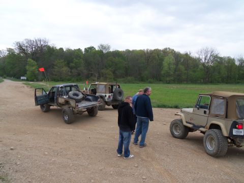 1989 Ford Bronco - A group of people and their off-road vehicles are gathered on a dirt path on an overcast day.