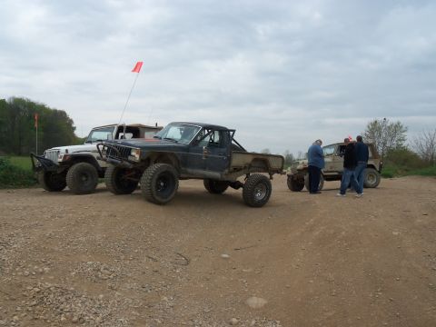1989 Ford Bronco - Several off-road vehicles are gathered on a dirt track under an overcast sky.