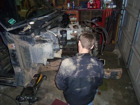 1968 Ford Bronco - Mechanic works on the front end of a vehicle in a garage, with the engine and chassis exposed.
