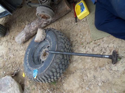 1989 Ford Bronco - An axle shaft is positioned across a large tire, with other vehicle parts and tools visible in the background.