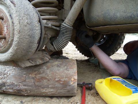 1989 Ford Bronco - Working on the rear suspension of a vehicle, with tools and a yellow fluid container nearby.