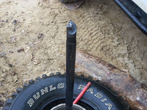 1989 Ford Bronco - A tire and a bent metal rod are visible on sandy ground, with a red tool nearby.