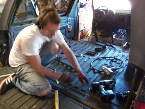 1968 Ford Bronco - A person works on the interior floor of a vehicle, surrounded by tools and disassembled parts.