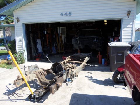 1968 Ford Bronco - A vehicle chassis and frame is being worked on in front of a garage containing another vehicle.