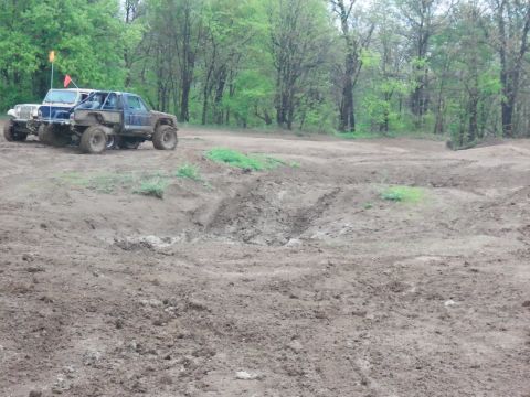 1989 Ford Bronco - Off-road vehicles are parked in a muddy field with trees in the background.