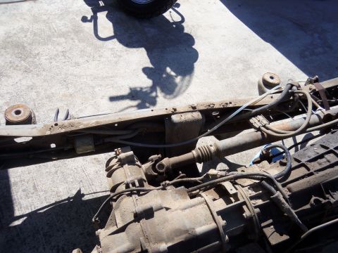 1968 Ford Bronco - Close-up view of a vehicle's chassis components, including the frame, transmission, and driveshaft, resting on a concrete surface.