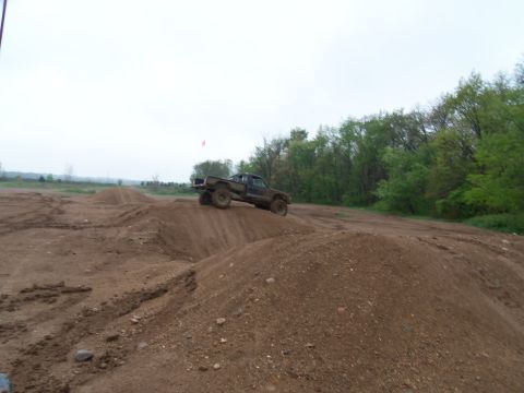1989 Ford Bronco - A pickup truck navigates a dirt track with mounds and trees under an overcast sky.