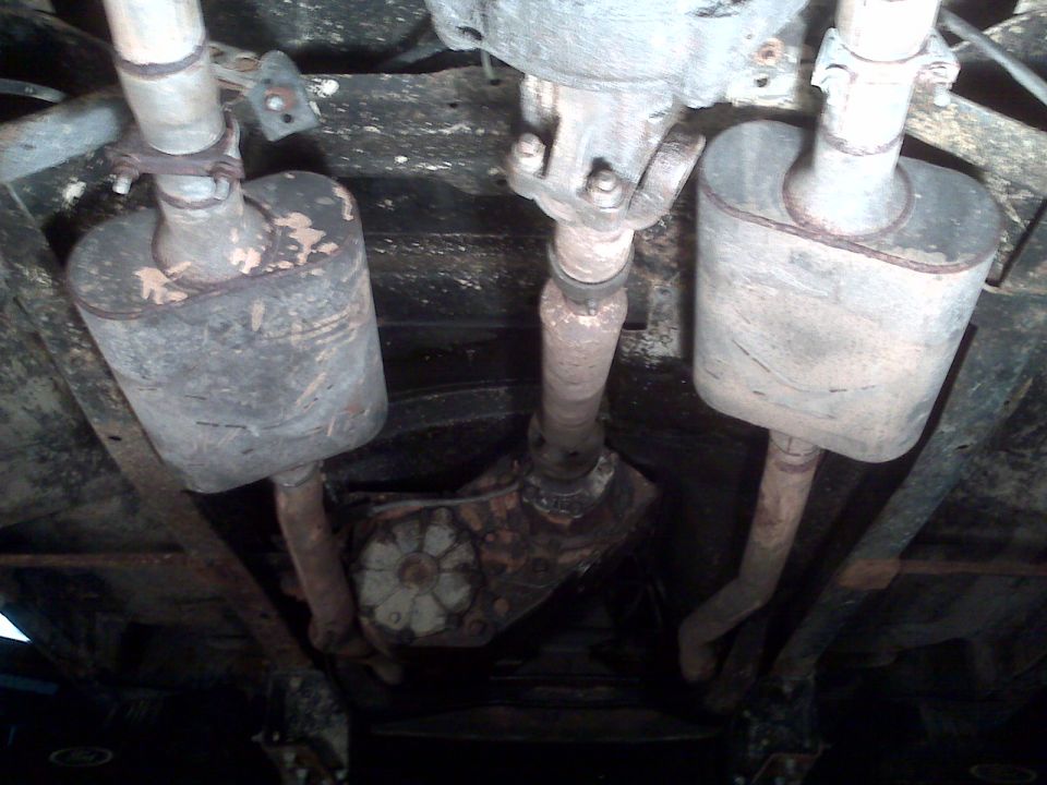 Underside view of a vehicle's dual exhaust system, showing mufflers and driveshaft