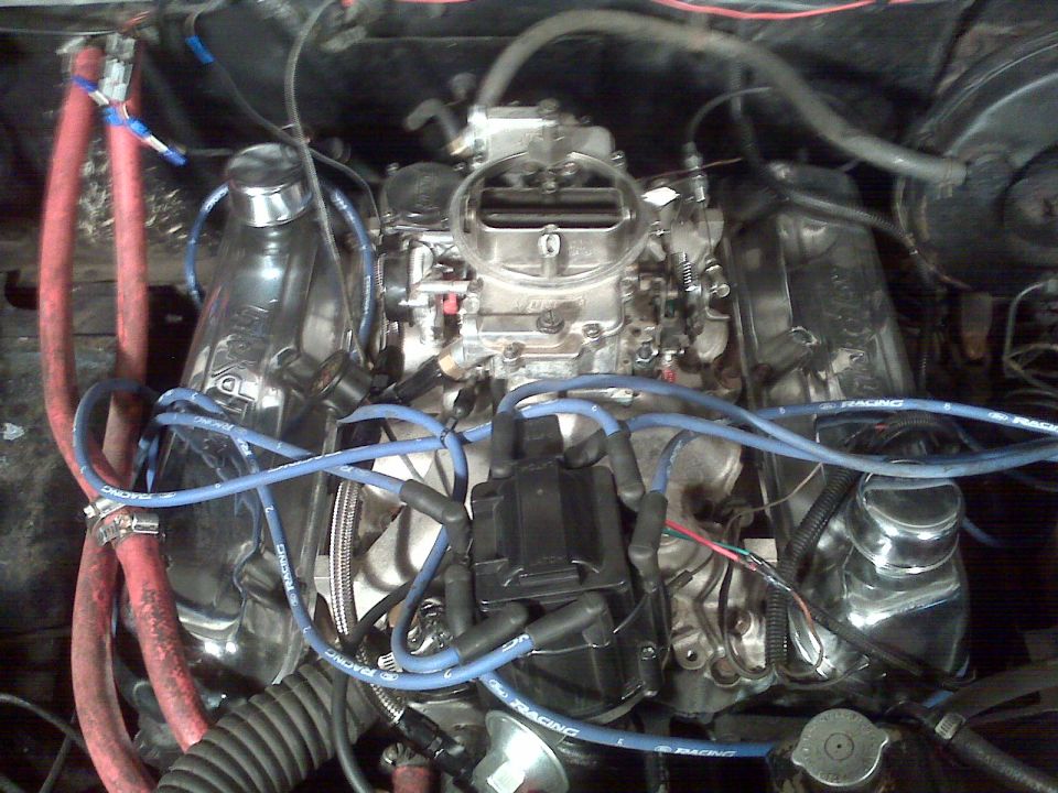 Close-up of engine bay with chrome valve covers, carburetor, and blue spark plug wires