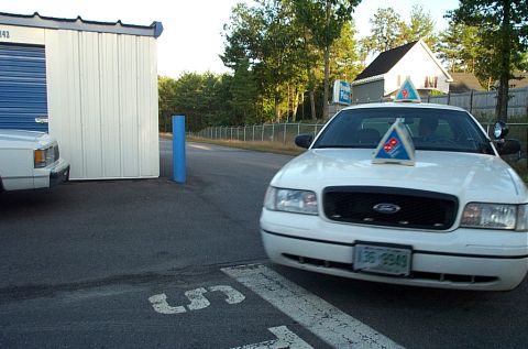2001 Ford Crown Victoria - A white 2001 Ford Crown Victoria, marked with Domino's pizza signs, is parked in front of a white storage unit.