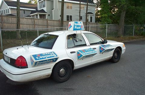 2001 Ford Crown Victoria - A white 2001 Ford Crown Victoria, branded with Domino's Pizza signage, is parked on a street.