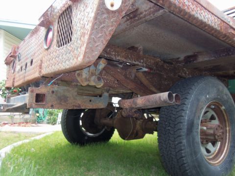 1968 Ford Bronco - The rear undercarriage of a heavily rusted truck shows dual exhaust pipes and leaf springs.