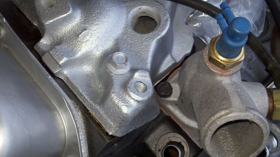 Close-up of a silver engine component with bolts and a brass fitting with blue plastic caps