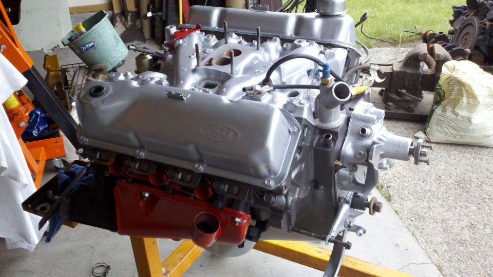 Silver Ford V8 engine on an orange engine stand, red oil pan, some hoses attached
