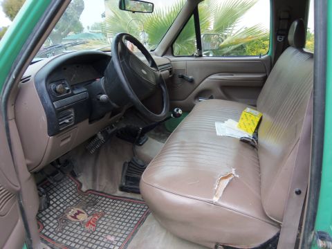 1968 Ford Bronco - The interior of a pickup truck features a worn passenger seat and a dashboard with a steering wheel and floor shifter.