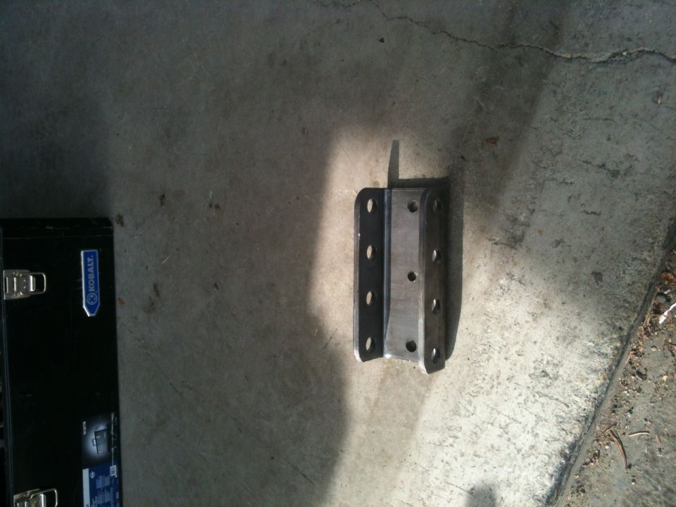 Metal bracket with multiple bolt holes, next to a black toolbox with a blue logo