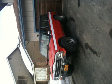 1990 Chevrolet Suburban - This red SUV, likely from the 1980s, is parked in front of a garage with its door partially open.