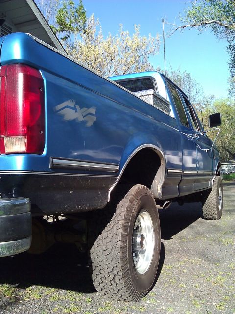 1992 Ford F-150 - A blue Ford F-150 pickup truck is parked outdoors on a sunny day, showing its rear and side profile.