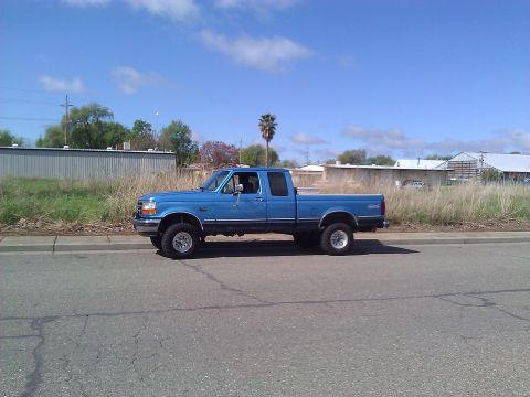1992 Ford F-150 - A blue 1992 Ford F-150 crew cab pickup truck is seen from the side, parked on a street with buildings in the background.