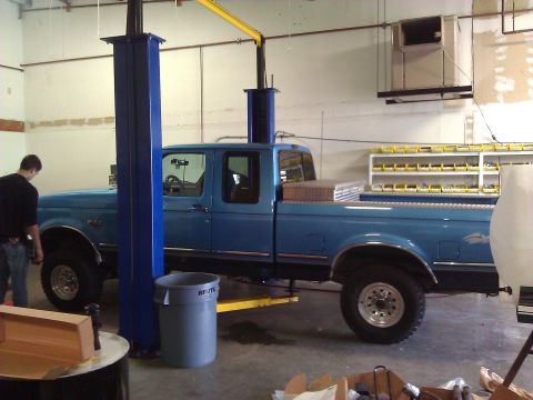 1992 Ford F-150 - A blue 1992 Ford F-250 truck is raised on a lift inside a workshop.