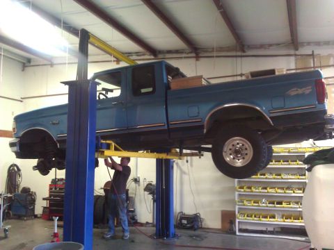 1992 Ford F-150 - A mechanic works on a blue 1992 Ford F-150 truck that is raised on a hydraulic lift inside a workshop.