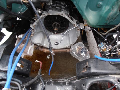 1990 Ford Bronco - Close-up view of a vehicle's transmission and engine bay, showing various mechanical parts and fluid leaks.