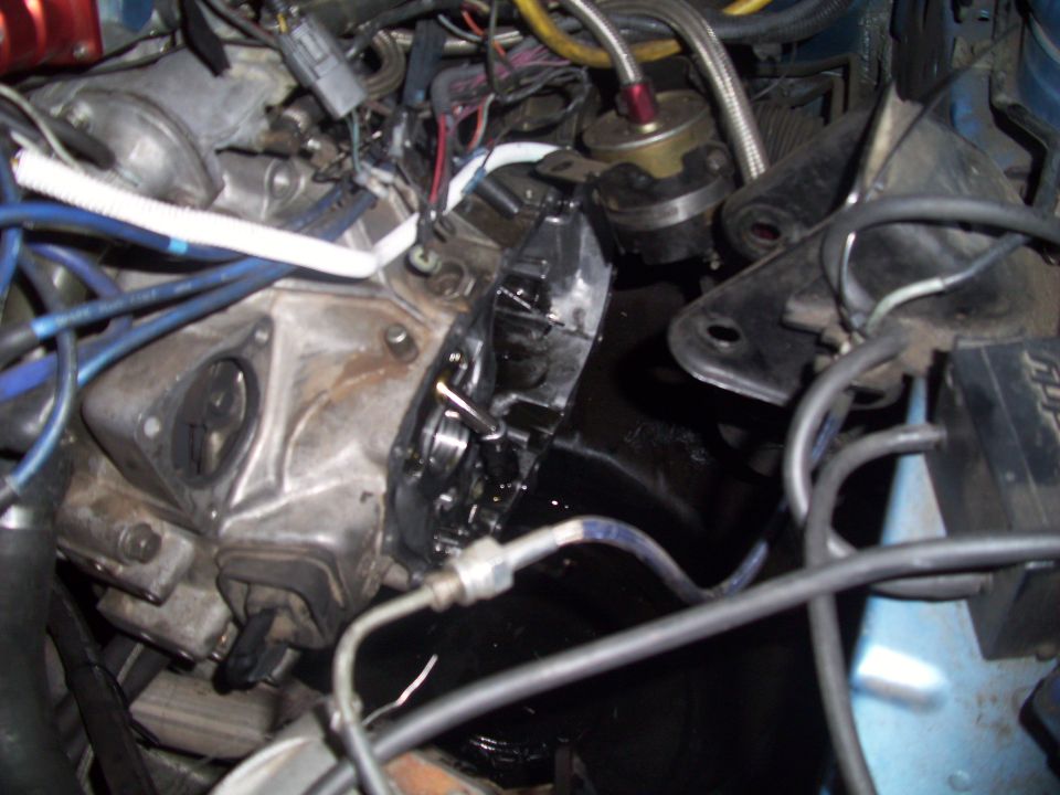 Engine bay with various hoses, wires, and metal components. A black fluid is visible