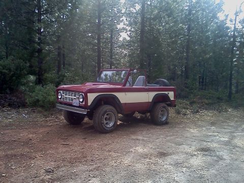 1968 Ford Bronco - This classic 1968 Ford Bronco, painted in a striking red and cream two-tone, is parked on a dirt road surrounded by trees.