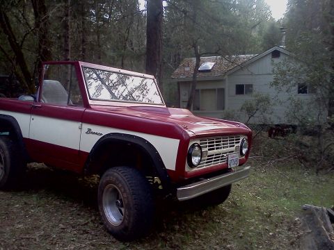 1968 Ford Bronco - A two-tone red and white 1968 Ford Bronco is parked in a wooded area near a house.