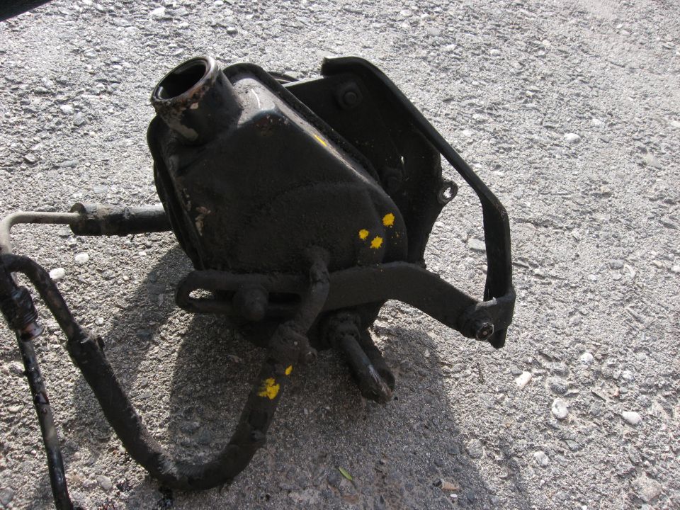 Black power steering pump with yellow paint marks and hoses, resting on gravel
