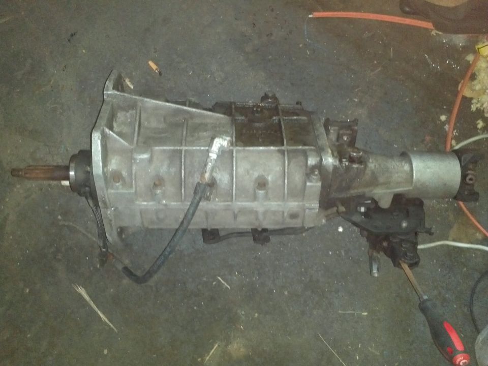 Aluminum automatic transmission with a metal shaft on the left and a silver housing on the right, resting on a dark floor